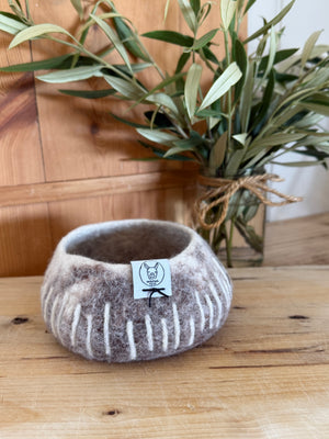 Felted bowl with a label on a wooden surface, next to a plant.
